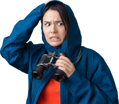 A tourist girl in a blue raincoat holds binoculars in her hands and looks into the distance, spies.