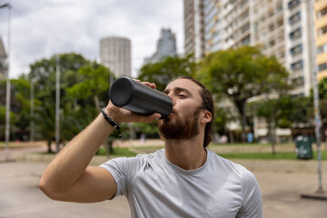 Brazil, Sao Paulo, Athletic man drinking from bottle after workout in city