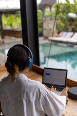 Woman sitting in hotel lounge and using laptop with headphones