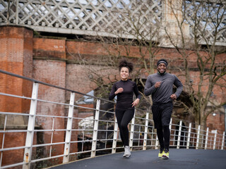 Smiling athletic man and woman jogging on footbridge