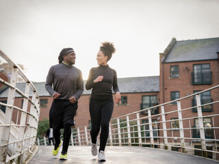 Smiling athletic man and woman jogging on footbridge