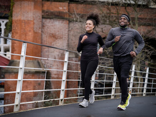 Smiling athletic man and woman jogging on footbridge