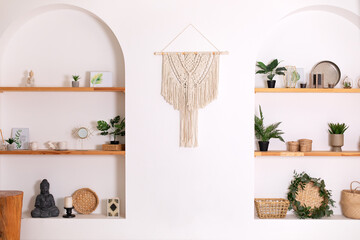 Modern composition of wabi sabi interior with shelf with home decoration and macrame. Stylish interior of living room and wall panel in style of Boho made of cotton threads using macrame technique