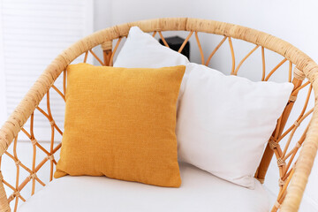 Design wicker wooden chair with pillows in stylish light bedroom interior. Rattan armchair by the...