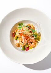 Elegant food - salad with shrimp and avocado on white table with harsh shadow. Flashy food concept. Seafood salad with shrimp, tomatoes and avocado on white plate with sunlight.