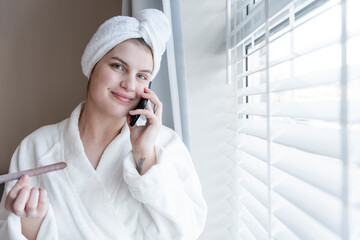Portrait of smiling woman in bathrobe and towel turban talking on smart phone