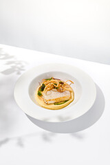 Roasted squid on mashed potatoes and crispy onion. Grilled squid with celery cream on white plate with shadows of leaves. Summer seafood menu. Roasted calamari in fine dining.