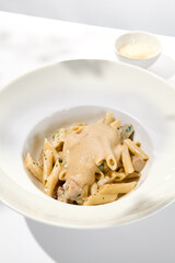 Italian pasta penne with chicken and mushrooms in creamy sauce. Mushroom and chicken pasta on white plate with shadows of sunlight. Summer italian lunch Penne with mushroom sauce on light background