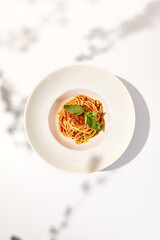 Vegetarian pasta with basil and tomatoes on white plate. Tomato pasta in summer menu with hard shadows Spaghetti with tomatoes on light background. Vegan food - spaghetti marinara
