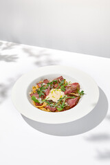 Homemade pasta with pastrami and creamy sauce with cheese. Italian pasta pappardelle with beef and sauce on white table Italian food in summer dining with shadows of sunlight
