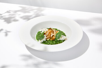 Green risotto with squid and stracciatella cheese on white plate. Creamy risotto with spinach,...