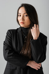 portrait of young asian businesswoman in black suit standing and looking at camera isolated on grey