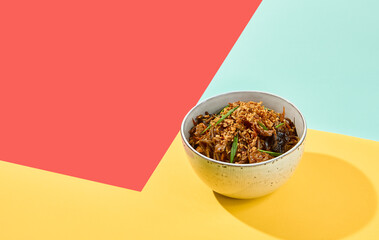 Asian fried buckwheat noodles with chicken on coloured background Fried noodles in ceramic bowl on yellow, red and blue background. Stir-fry soba in trendy style with shadows. Vibrant food