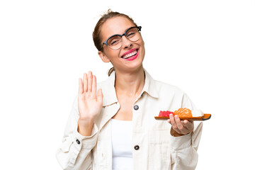 Young caucasian woman holding sashimi over isolated background saluting with hand with happy expression
