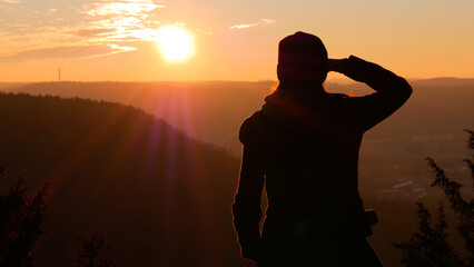 Silhouette of young person looking at view of mountains and setting sun.