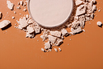 Crushed face powder heap and round box of pressed one on top on brown background, close up