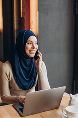 Young muslim woman using phone and working on computer in a cafe