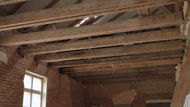 View of old ceiling wooden beams of spacious old red brick building during renovation. Old and dusty wood in cracks, no floor on abandoned attic floor.
