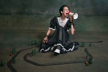 Shouting in megaphone. Young beautiful woman in image of Anna Karenina in retro black dress posing...