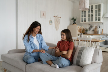 Cheerful caring woman trying to cheer up embarrassed school age daughter after house arrest. Shy...
