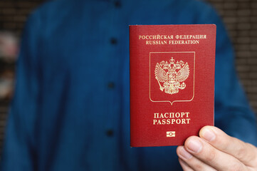 men's hands hold a red foreign Russian passport against the background of themselves in a shirt, their faces are not visible. close-up