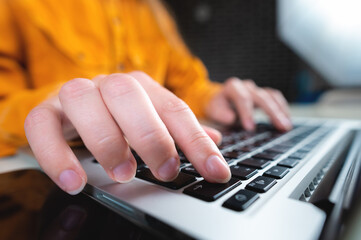 Hands of a woman working with a laptop in a home interior or office, close-up on a blurred background