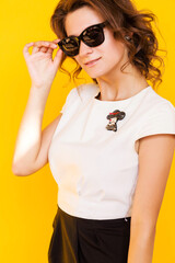 A brooch in the form of a lady in a hat on a white blouse of a brunette girl. Young woman posing on yellow background, sunlight and shadow in studio