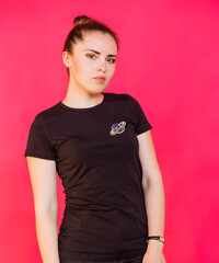 A girl in a black T-shirt with a brooch in the form of a planet with rings poses against a fuchsia...