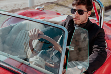 young man in convertible car looking at camera, smiling, man wears suit and tie drives red convertible car
