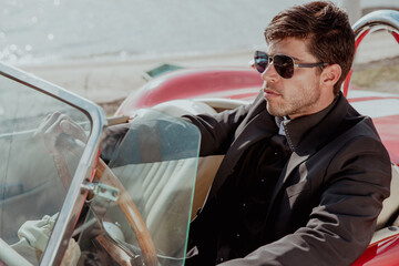 young man in convertible car looking at camera, smiling, man wears suit and tie drives red convertible car