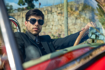 young man in convertible car looking at camera, smiling, man wears suit and tie drives red convertible car