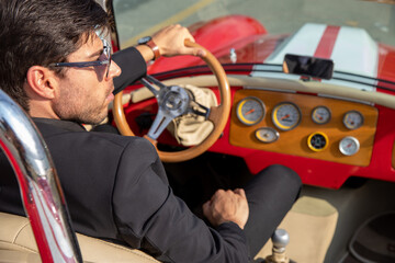 young man in convertible car looking at camera, smiling, man wears suit and tie drives red convertible car