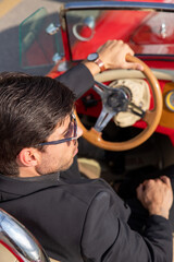 young man in convertible car looking at camera, smiling, man wears suit and tie drives red convertible car