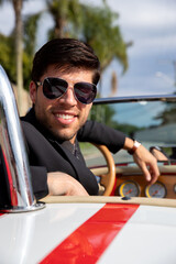 young man in convertible car looking at camera, smiling, man wears suit and tie drives red convertible car, person driving a car