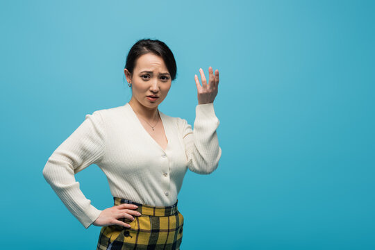 Confused Asian Woman In Cardigan Looking At Camera Isolated On Blue