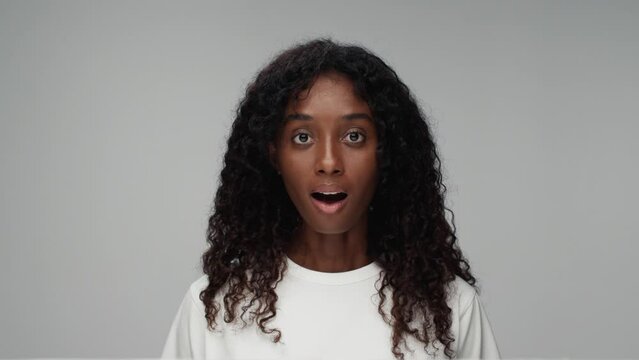 Portrait of Young Black Woman Looking Excited at Camera in Colour Studio Shot. Happy Girl with Wow Facial Expression Isolated Alone on Grey Background Close-up. Surprise for African American Person 4k