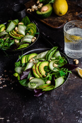 Salad of greens, cucumber and avocado on a dark table. Vegetarian dish