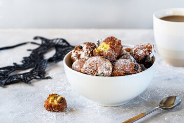 Italian traditional Carnival fritters toped with sugar powder in white bowl over concrete background with carnival mask, cacao mug and tea spoon