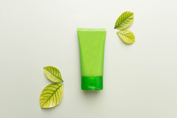 Natural herbal skincare products mock up. Top view of green squeeze bottle plastic tube with fresh leaves on green background. Packaging of lotion, cream, facial foam, gel, soap or shampoo.
