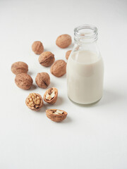 Dairy free substitute milk concept. Small glass bottle with vegetable walnut drink. Some shelled and opened nuts on the side.