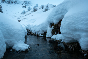 Ribeiro de água pela montanha abaixo rodeado por um grande manto de neve nos Pirenéus...