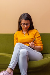 Casually dressed young Hispanic woman sitting on a sofa using a graphics tablet