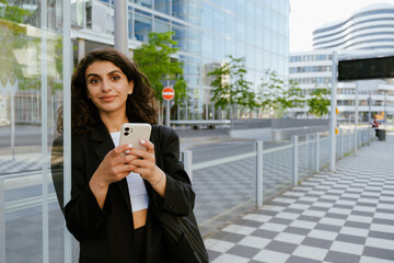 Fototapeta premium Young brunette woman smiling and using mobile phone on city street