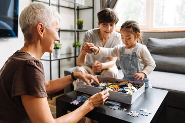 Two grandmothers collecting puzzles with their cute asian granddaughter