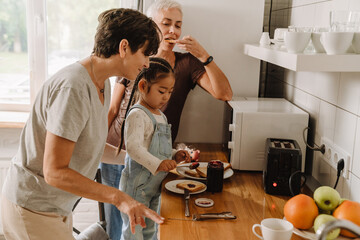 Happy family with cute little asian girl eating toasts - obrazy, fototapety, plakaty