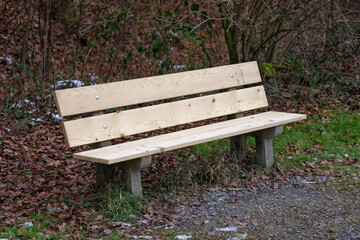 Empty wooden bench at border of gravel rural road at border of forest at City of Z&uuml;rich district Schwamendingen on a gray and cloudy winter day. Photo taken January 29th, 2023, Zurich, Switzerland.