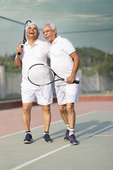 Active senior tennis players meeting at the net after a match and talking.