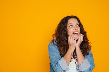 Excited girl touching her face and looking up isolated over yellow background