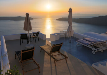 Sun loungers on terrace in the village of Imerovigli with amazing view of sunset over caldera in...