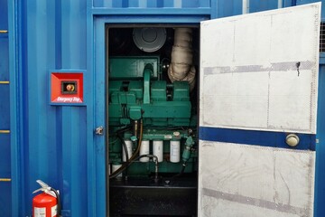 Open door of blue power pack or portable generator for supply of electricity to reefers transported on container vessel. Behind door is green diesel generator.